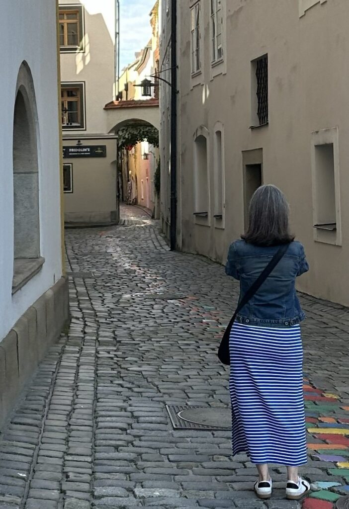 Julianne Sharpe stands with her back to the camera on a small European lane.